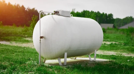 Technicien professionnel inspectant une citerne de gaz propane aérienne installée dans le jardin d'une maison individuelle française